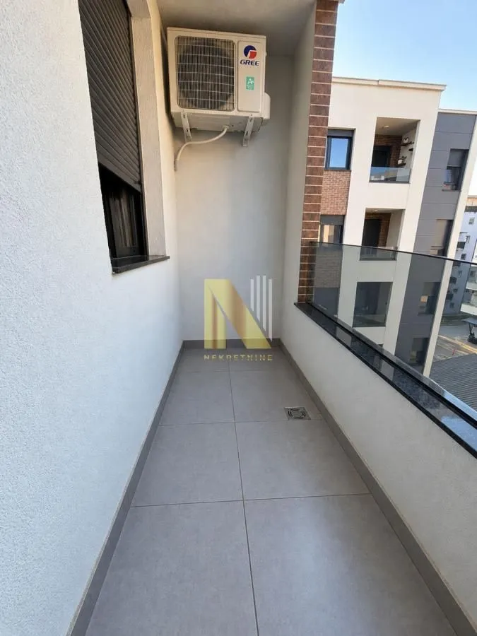 Pogled na prostrani balkon sa staklenom ogradom i klima uređajem.