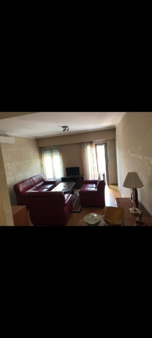 Living room with a red leather sofa set and a television by the window.