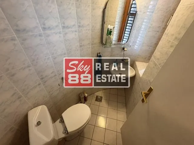 Small tiled bathroom equipped with a toilet, sink, and mirror.
