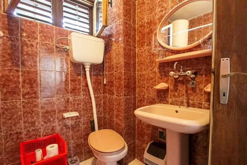 Kupatilo sa smeđim pločicama, lavaboom i ogledalom.