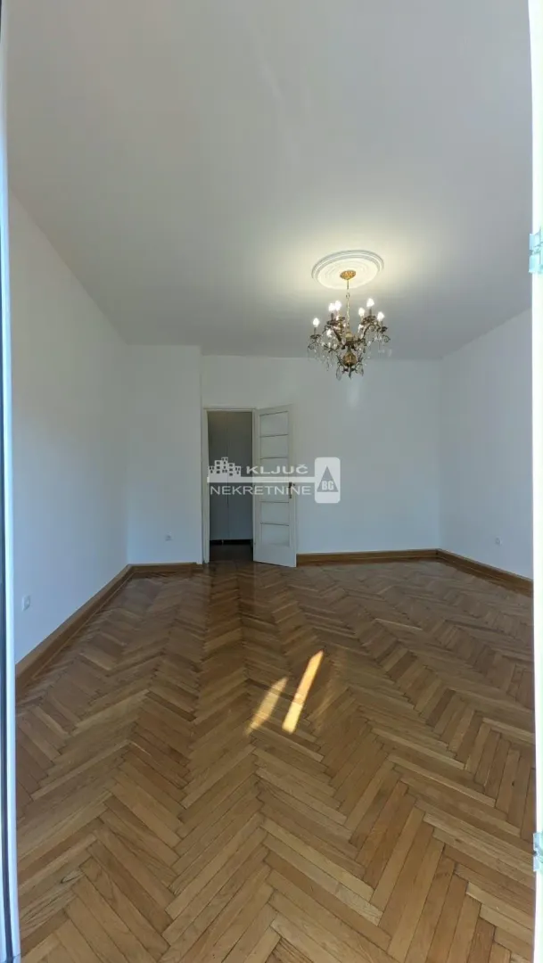 Empty room with hardwood parquet flooring and a chandelier on the ceiling.