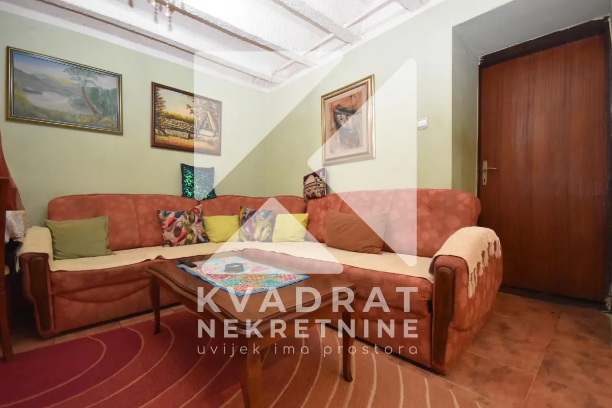 Dnevna soba sa ugaonom garniturom, klub stolićem i slikama na zidu.
