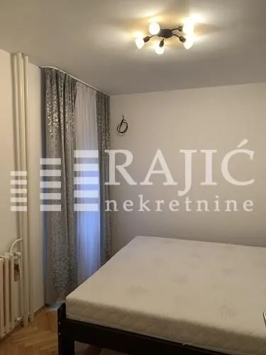 Spavaća soba sa bračnim krevetom i prozorom sa zavesama.
