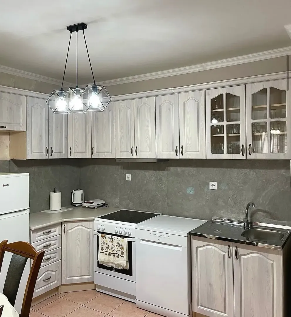 Kitchen with light wooden cabinets, stove, refrigerator, and sink.