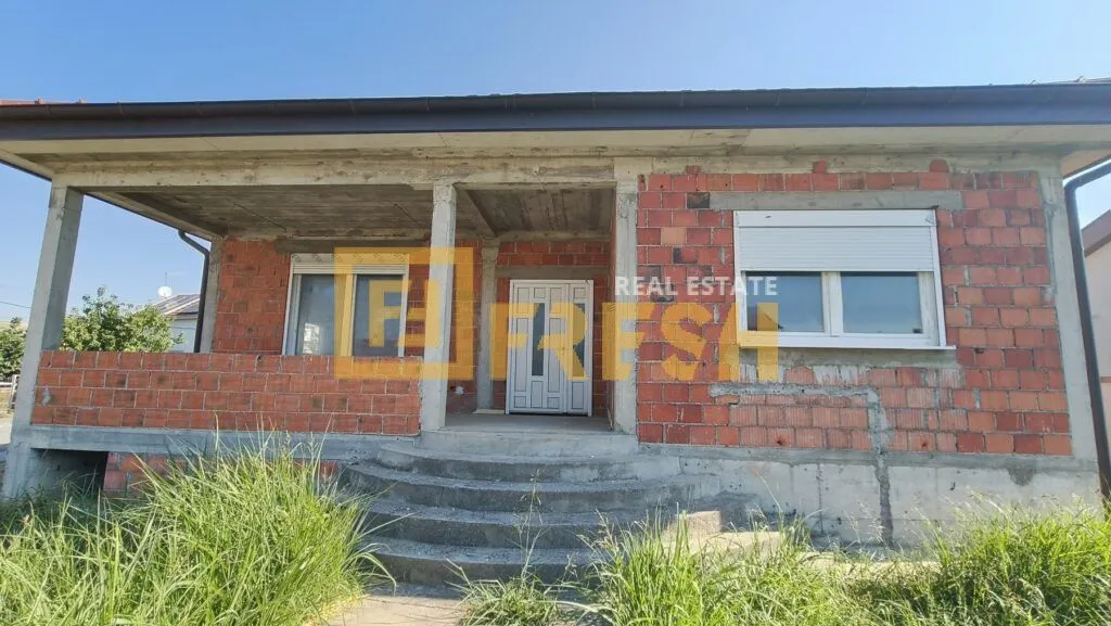 Prednji pogled na nedovršenu kuću od cigle sa ulaznim vratima i stepeništem.