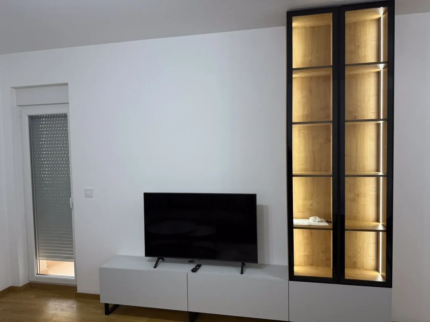 Dnevna soba sa modernom TV komodom, televizorom i osvijetljenom vitrinom.