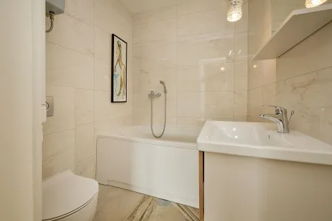 Kupatilo opremljeno kadom, umivaonikom i toaletom u svijetlim keramičkim pločicama. - image 6