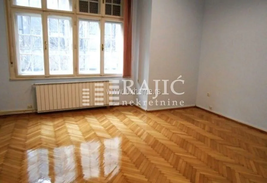Empty room with parquet flooring and large windows.