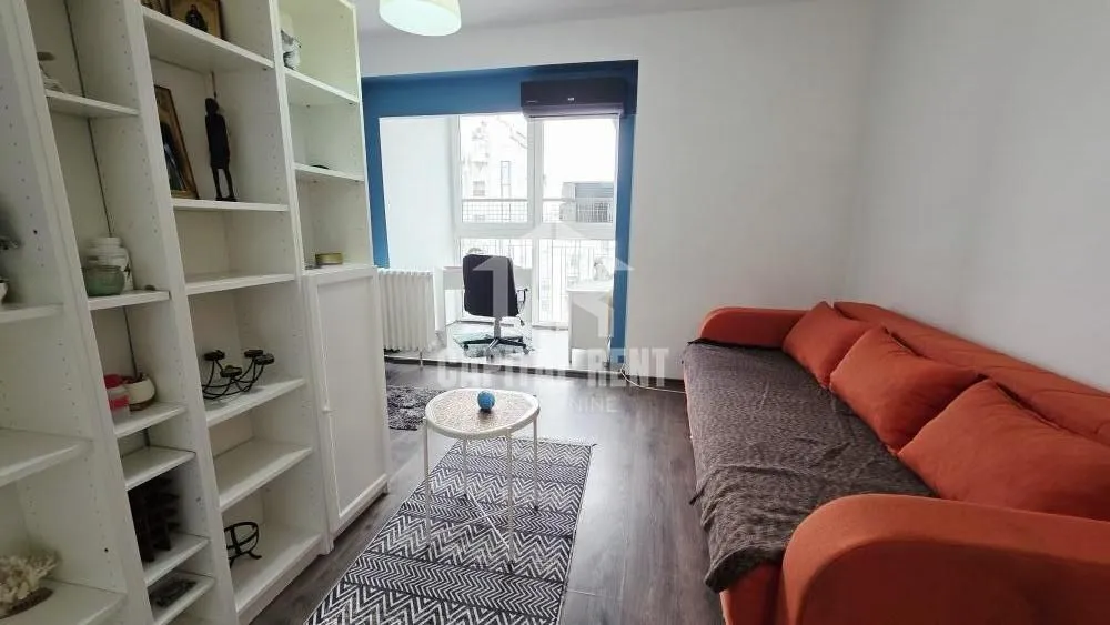 Living room with an orange sofa, white shelving unit, and access to the balcony.