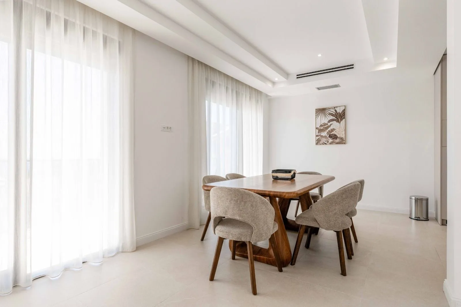 Dining area with a wooden table and upholstered chairs near large windows.