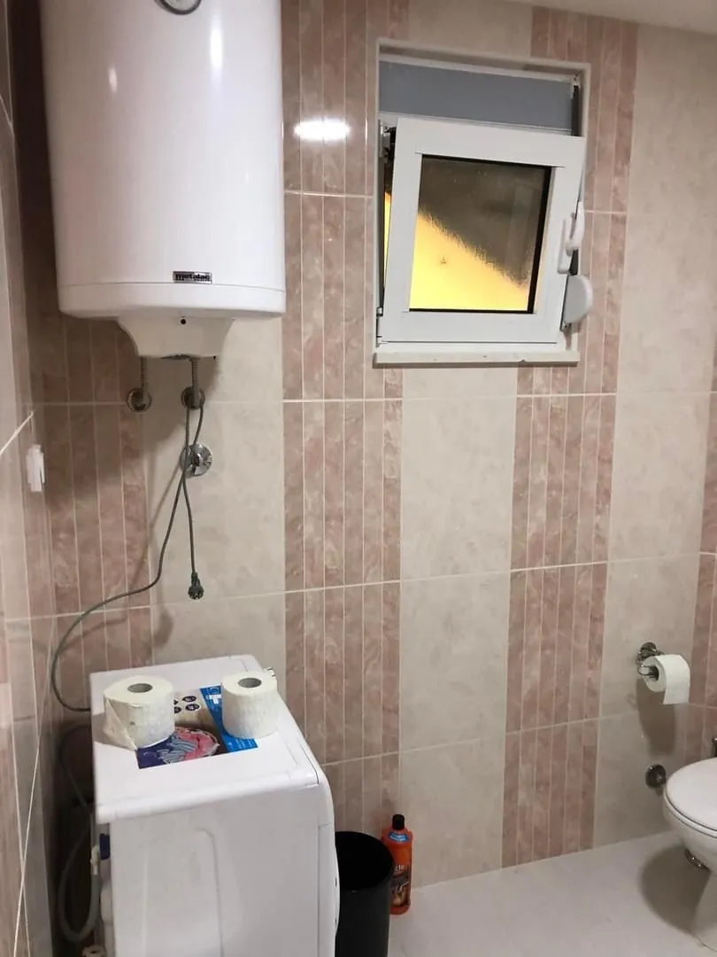 Small bathroom with brown-toned tiles, a water heater, washing machine, and sanitary fixtures.