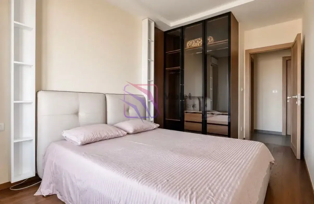 Furnished bedroom with a double bed, built-in wardrobe, and white shelving units.