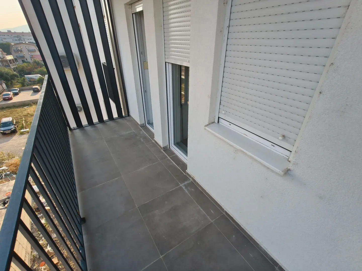 View of a spacious balcony with dark tiles and a metal railing.