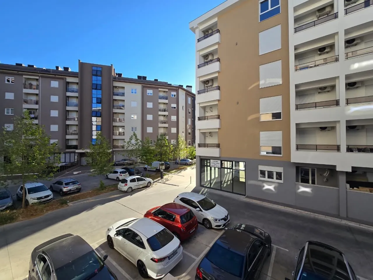 Pogled sa terase na zgrade i parking ispred stambenog kompleksa.