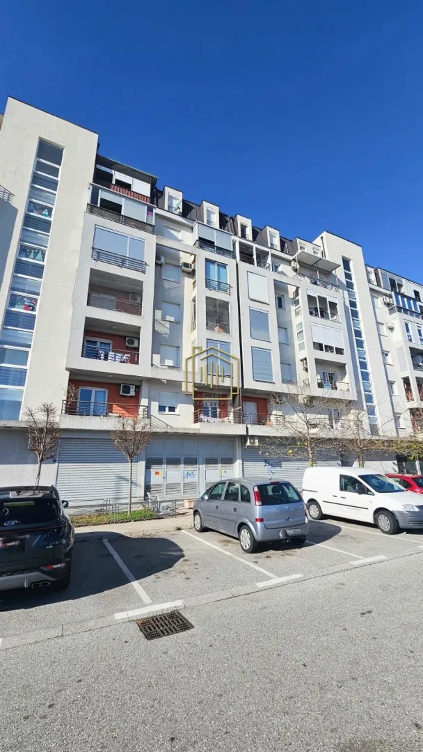 Pogled na spoljašnjost stambene zgrade sa parkingom.
