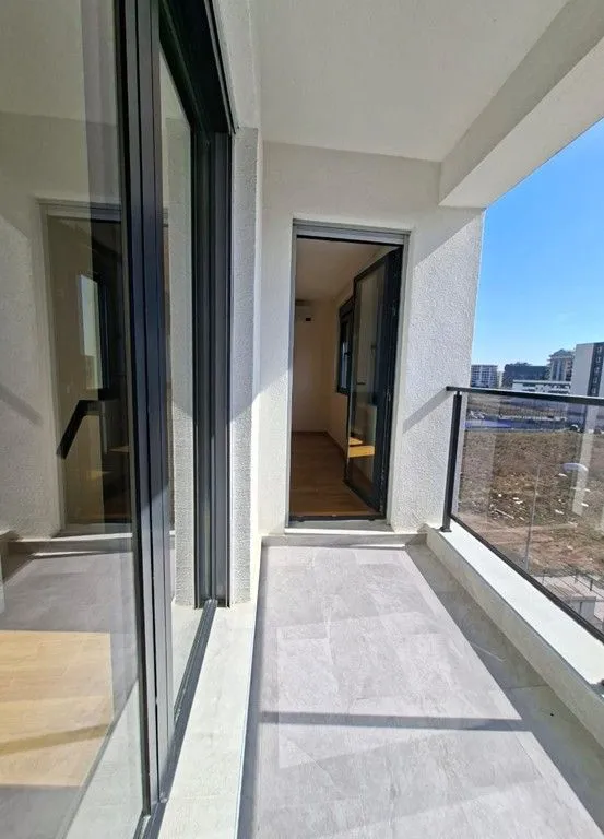 Nenamješten balkon sa staklenom ogradom i pogledom na okolinu.