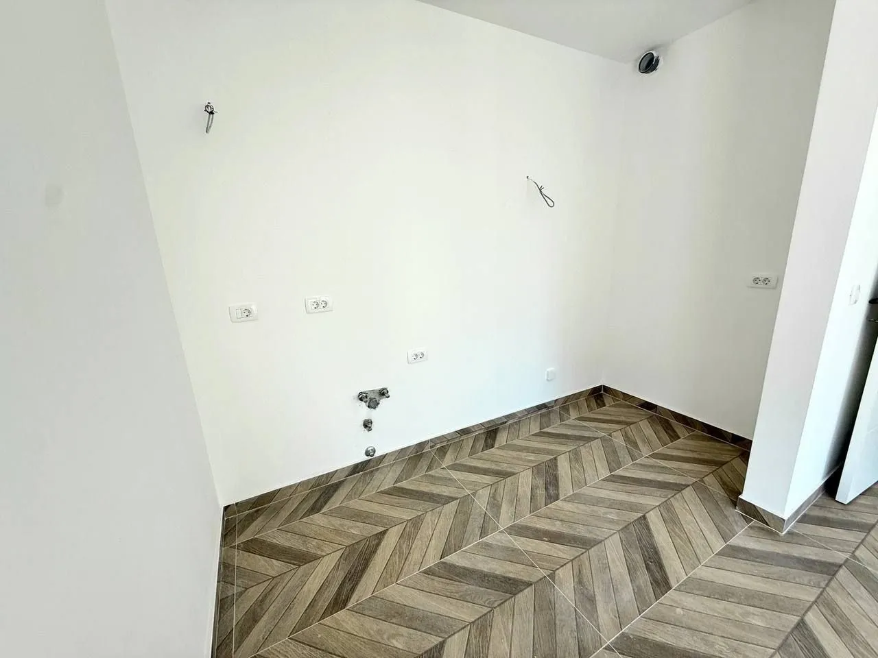 Empty room with ceramic floor tiles and water and electrical connections.