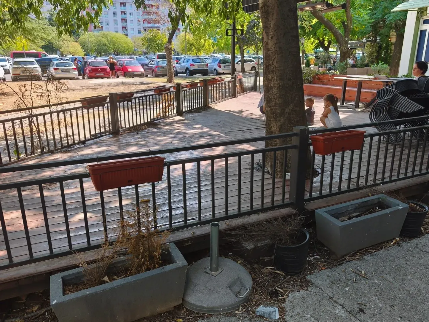 View of the fenced terrace with a wooden floor and a view of the parking lot and surrounding buildings.