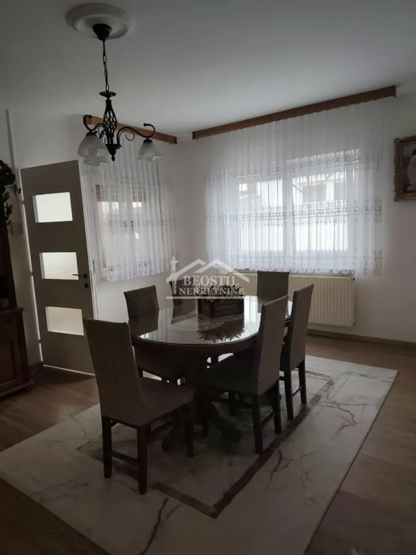 Trpezarija sa stolom i stolicama, prozorom i lusterom.