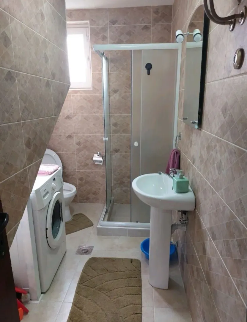 Manje kupatilo sa tuš kabinom, umivaonikom, veš mašinom i toaletom.