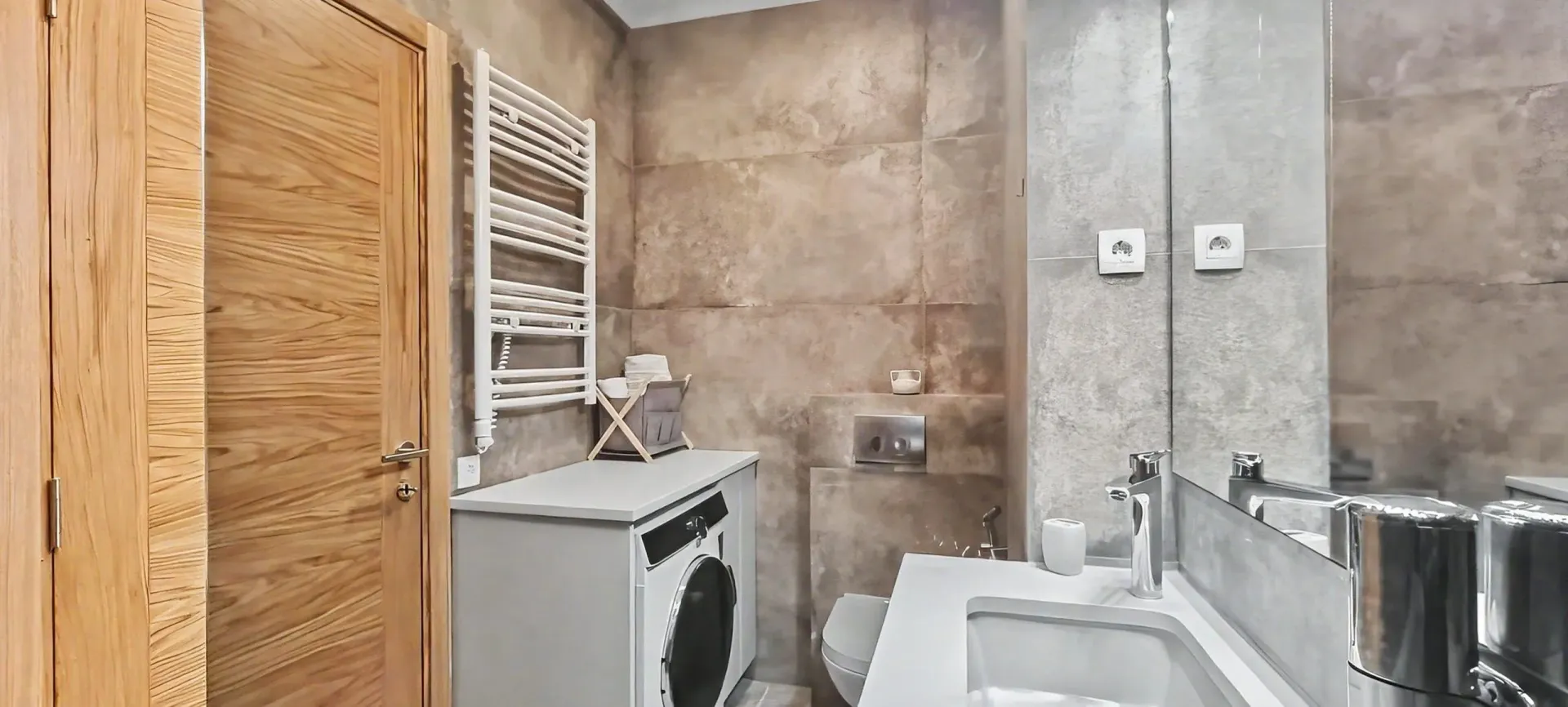 Moderno opremljeno kupatilo sa veš mašinom i velikim ogledalom.