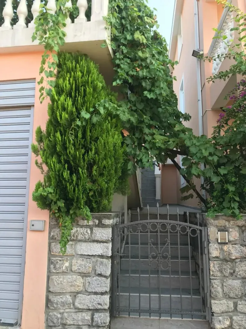 Ulaz u dvorište kuće sa kamenom ogradom, kapijom i zelenilom.