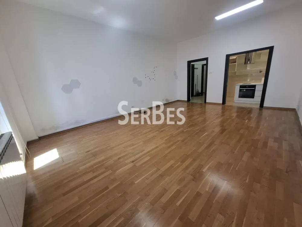Empty living room with parquet flooring and a view of the kitchen.