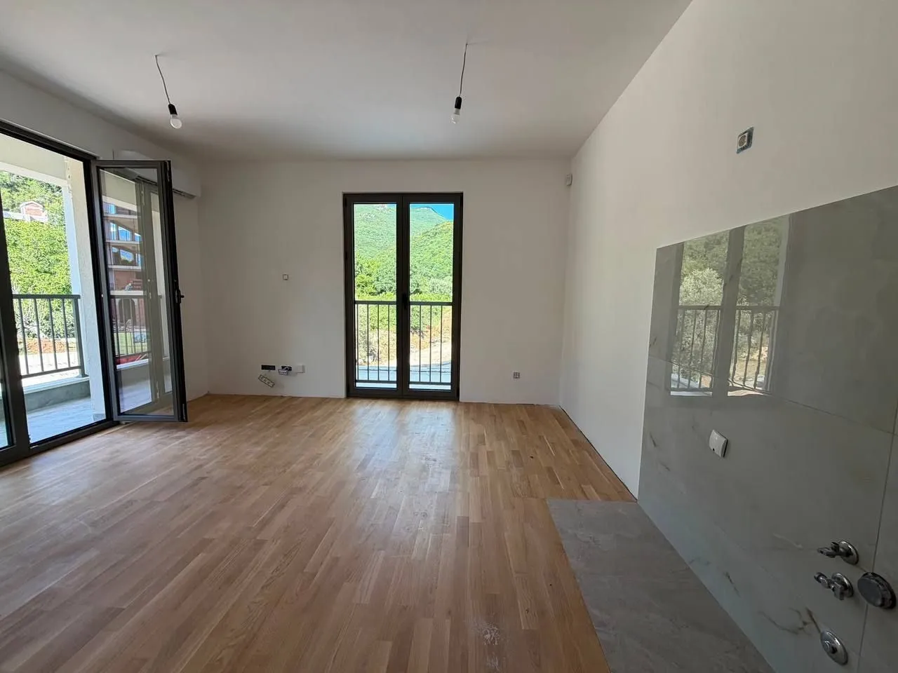 Prazna soba sa parketom i izlazom na balkon i terasu.