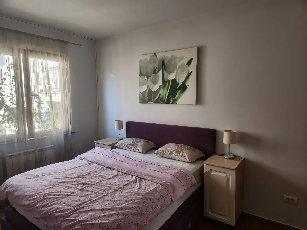 Namještena spavaća soba sa bračnim krevetom, noćnim stočićima i prozorom.