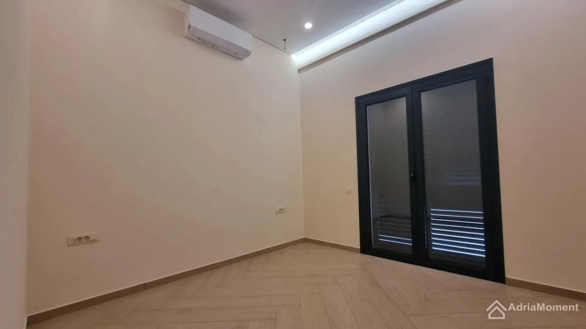Prazna soba sa laminatom i balkonskim vratima.