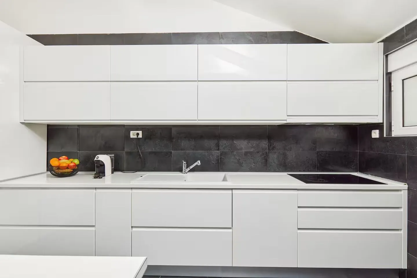 Modern kitchen with white units and dark tiles.