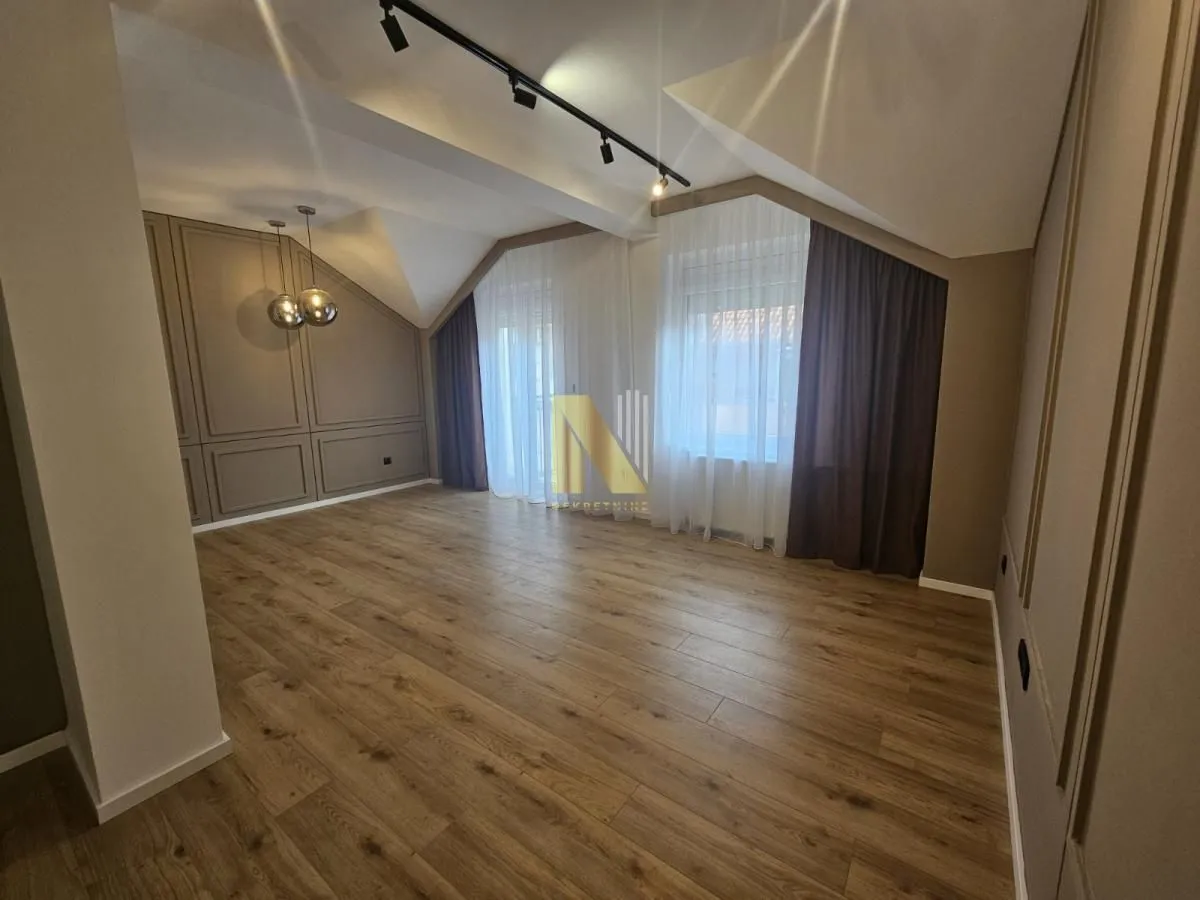 Prazna dnevna soba sa drvenim podom, spuštenim plafonom i osvetljenjem.