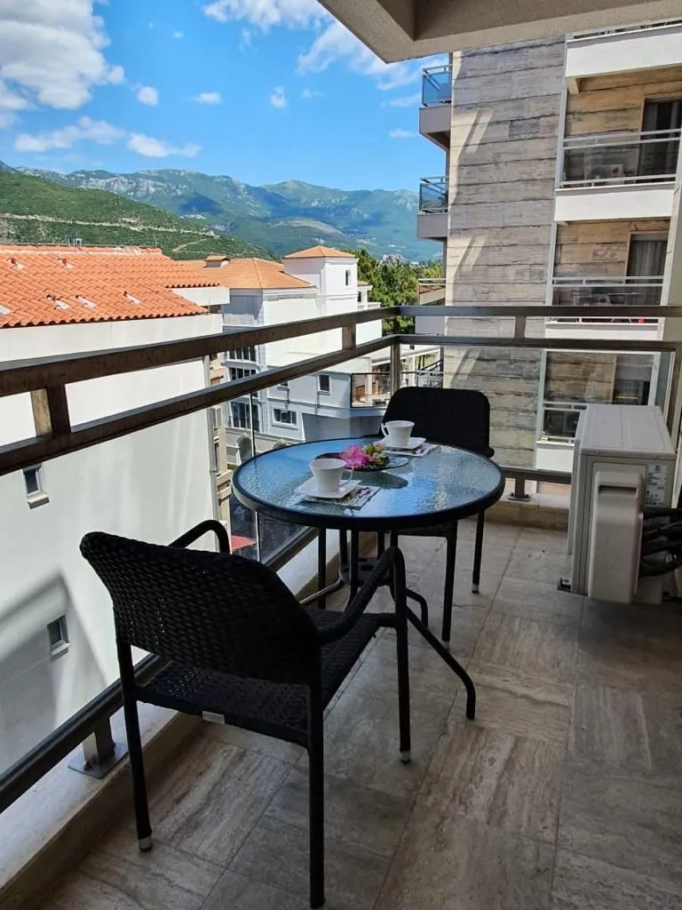 Furnished terrace with a table, chairs, and a view of surrounding buildings and mountains.