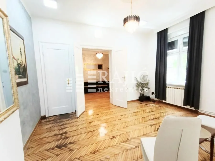 Spacious living room with hardwood parquet flooring and an open passageway to another room.