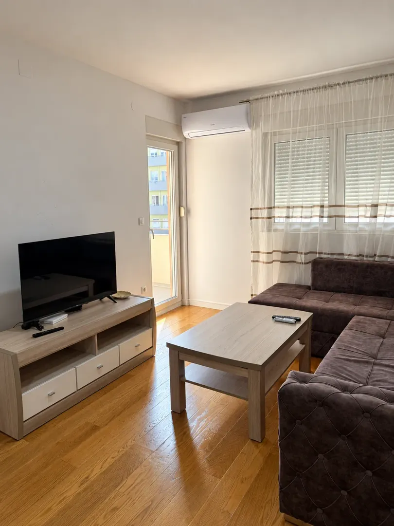 Living room with a corner sofa, television, and air conditioning unit.
