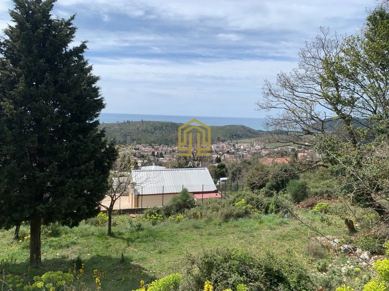 Pogled iz dvorišta na okolni pejzaž i naselje sa morem u pozadini.