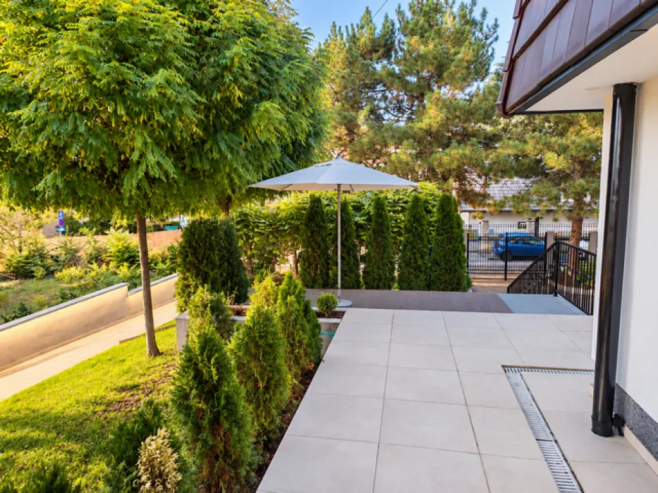 Paved courtyard with a parasol and landscaped greenery around the house.