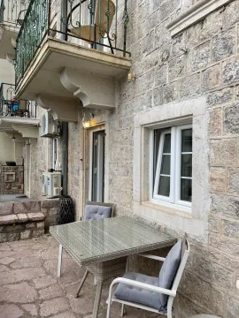 Stone facade of a building with a balcony and a table with chairs in the courtyard. - image 12