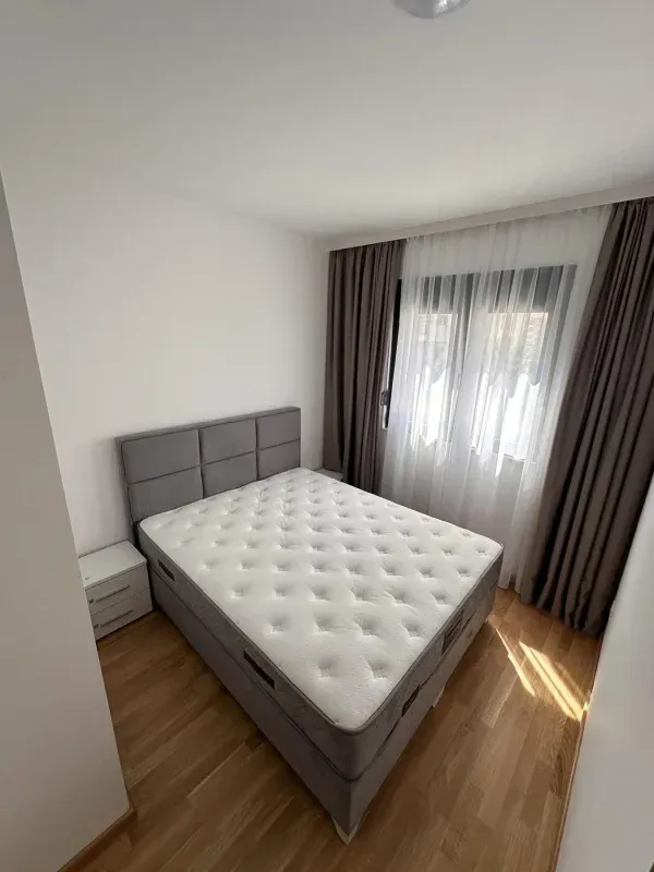 Svjetla spavaća soba sa bračnim krevetom, bijelim noćnim ormarićima i prozorom sa zavjesama.