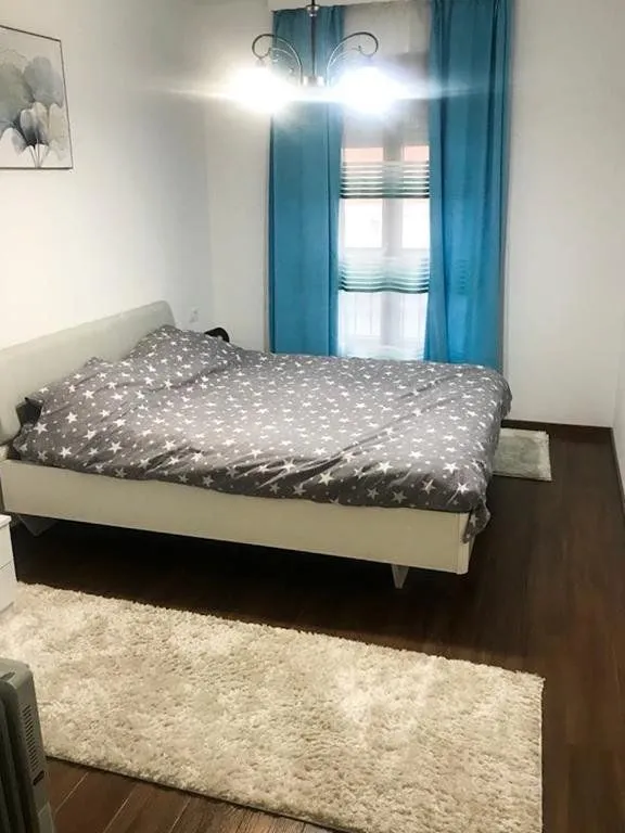 Namještena spavaća soba sa bračnim krevetom, plavim zavjesama i tepisima.