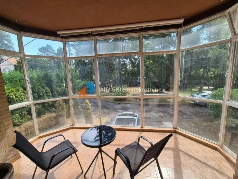 Enclosed terrace with seating furniture and a view of greenery.