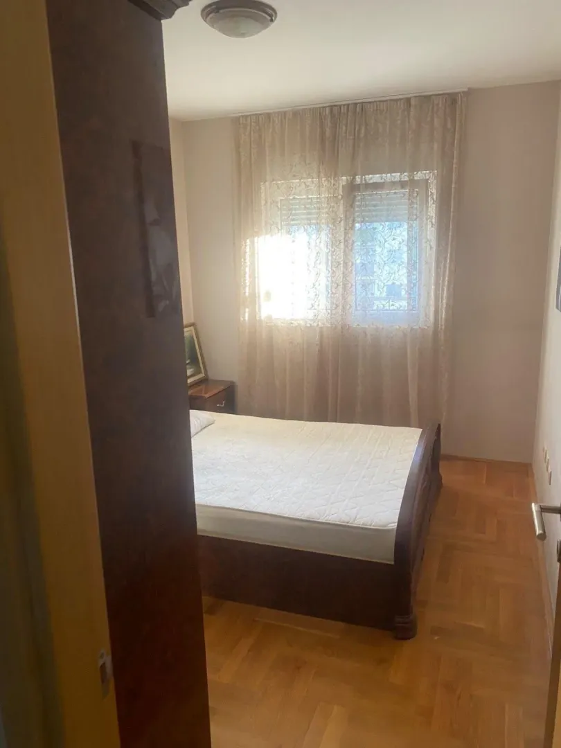 Manja spavaća soba sa bračnim krevetom i prozorom sa zavjesama.