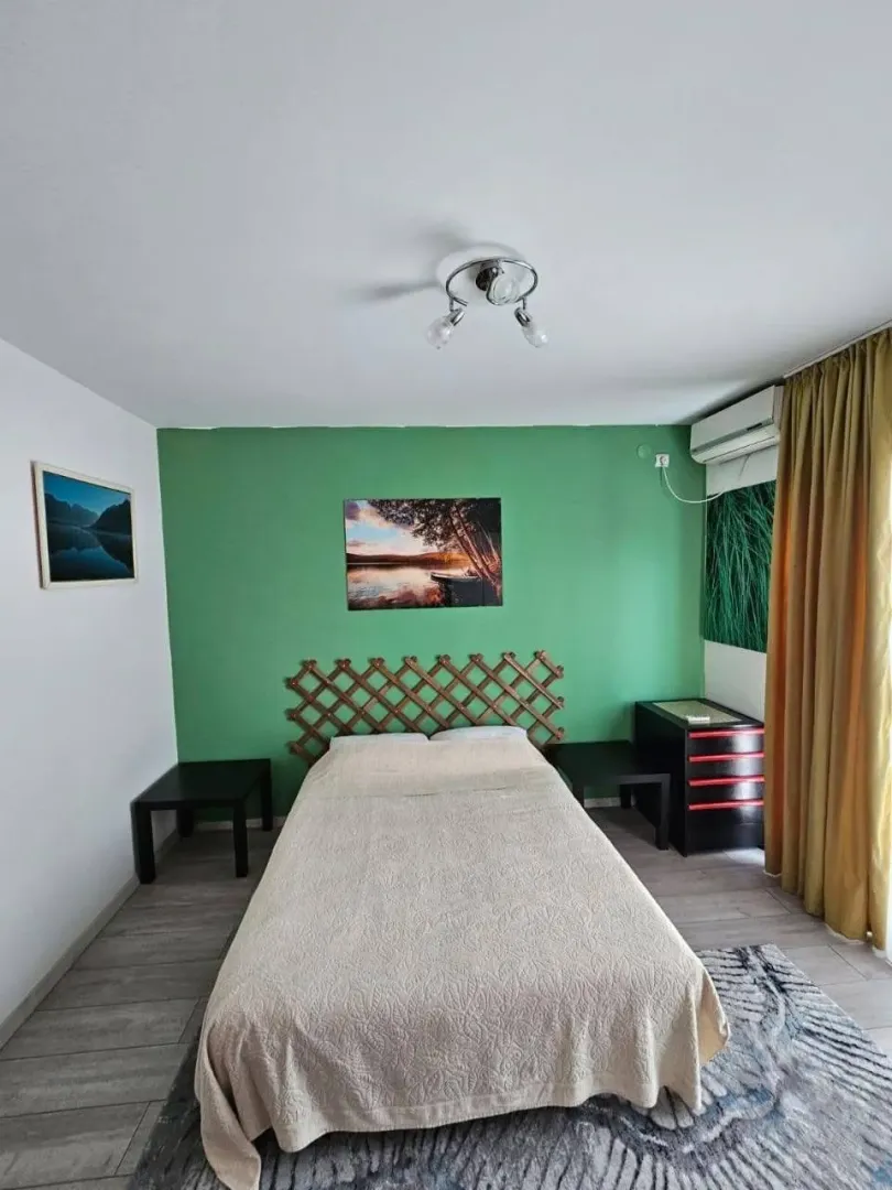Furnished bedroom with a double bed, green feature wall, and air conditioning.