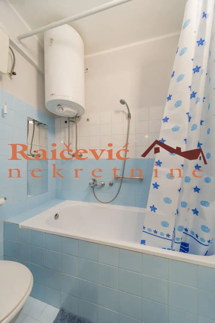 Small bathroom with a bathtub, blue tiles, and a wall-mounted water heater.