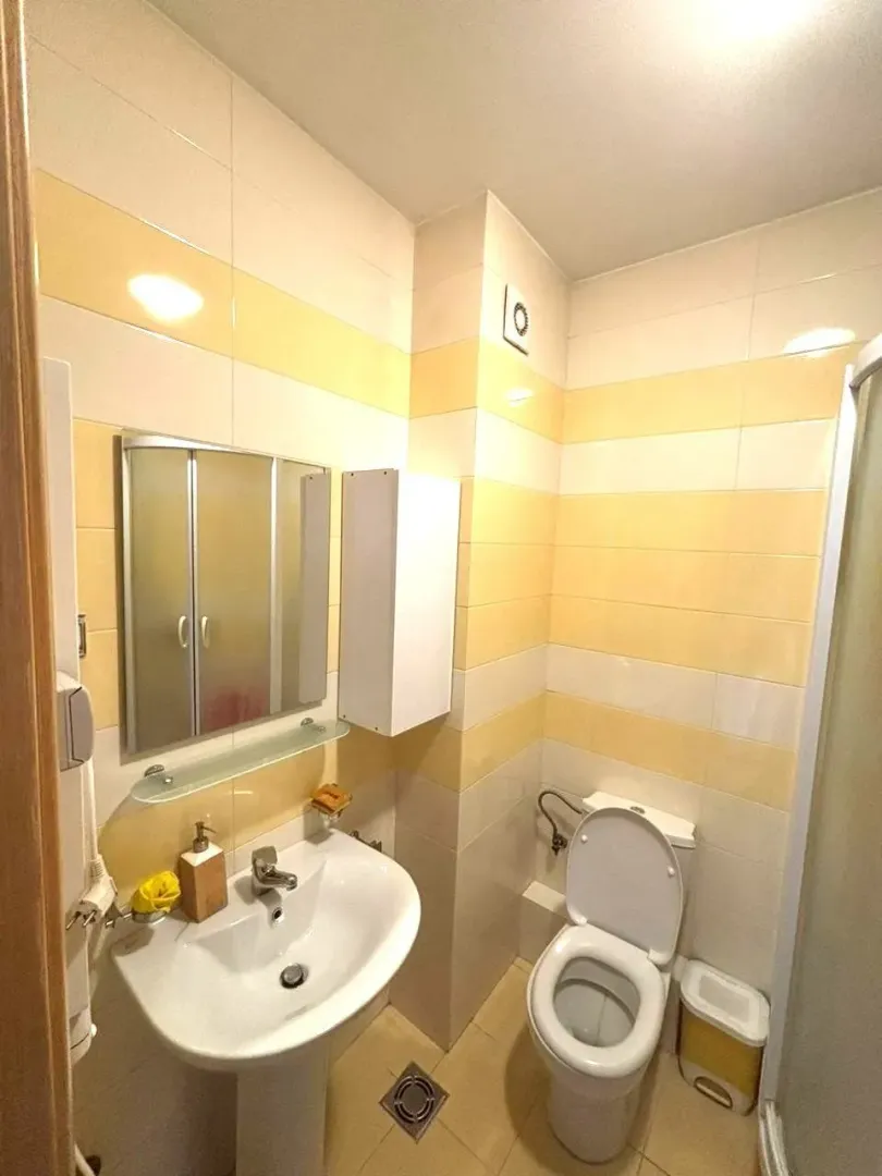Bathroom equipped with a sink, mirror, toilet, and shower cabin with yellow and white tiles.