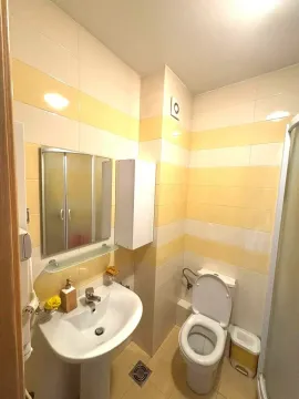 Bathroom equipped with a sink, mirror, toilet, and shower cabin with yellow and white tiles. - image 3