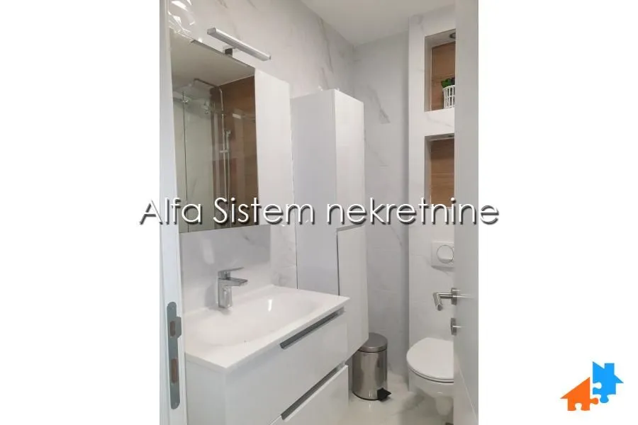 Moderno kupatilo sa belim elementima i mermernim pločicama.