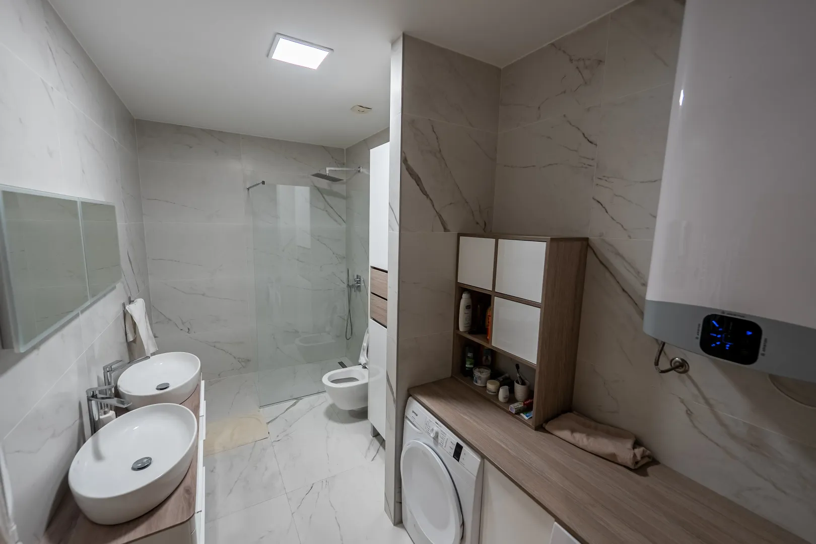 Modern bathroom with two washbasins, a walk-in shower, and a built-in washing machine.