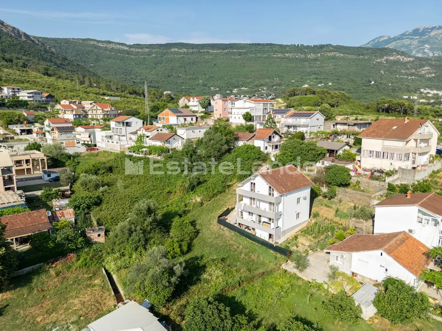 Pogled iz vazduha na kuću i okolno naselje u zelenilu.
