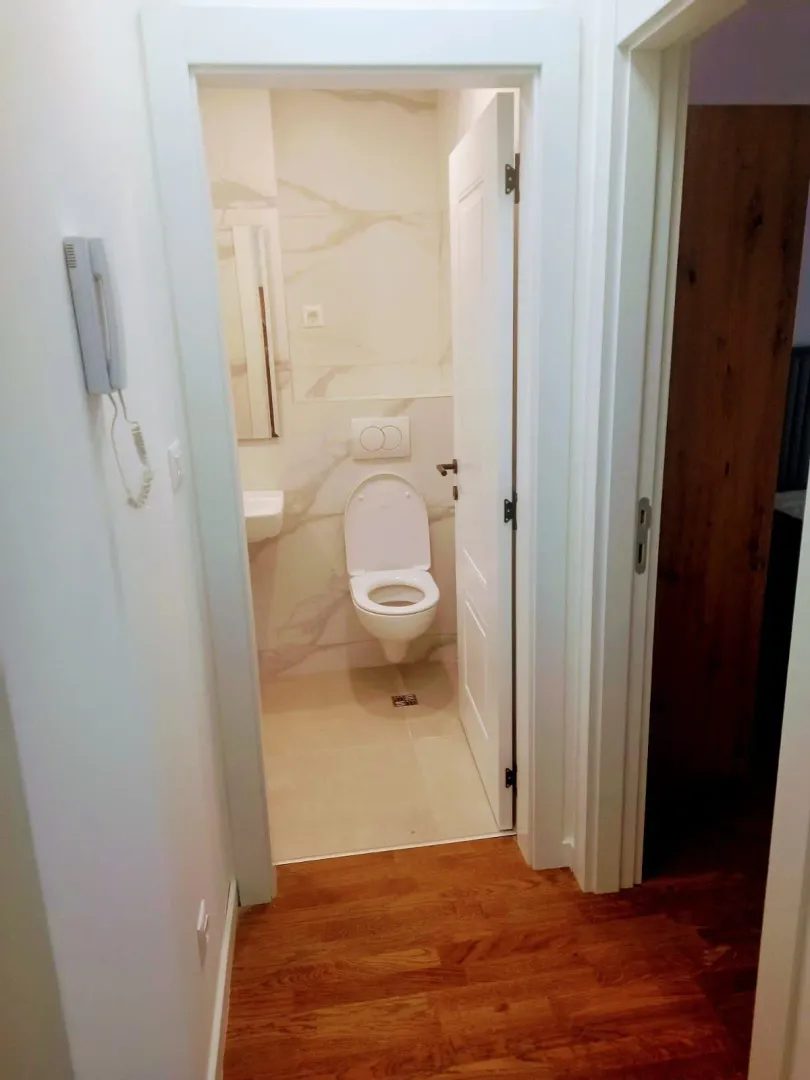 Pogled iz hodnika na kupatilo sa WC šoljom i umivaonikom.